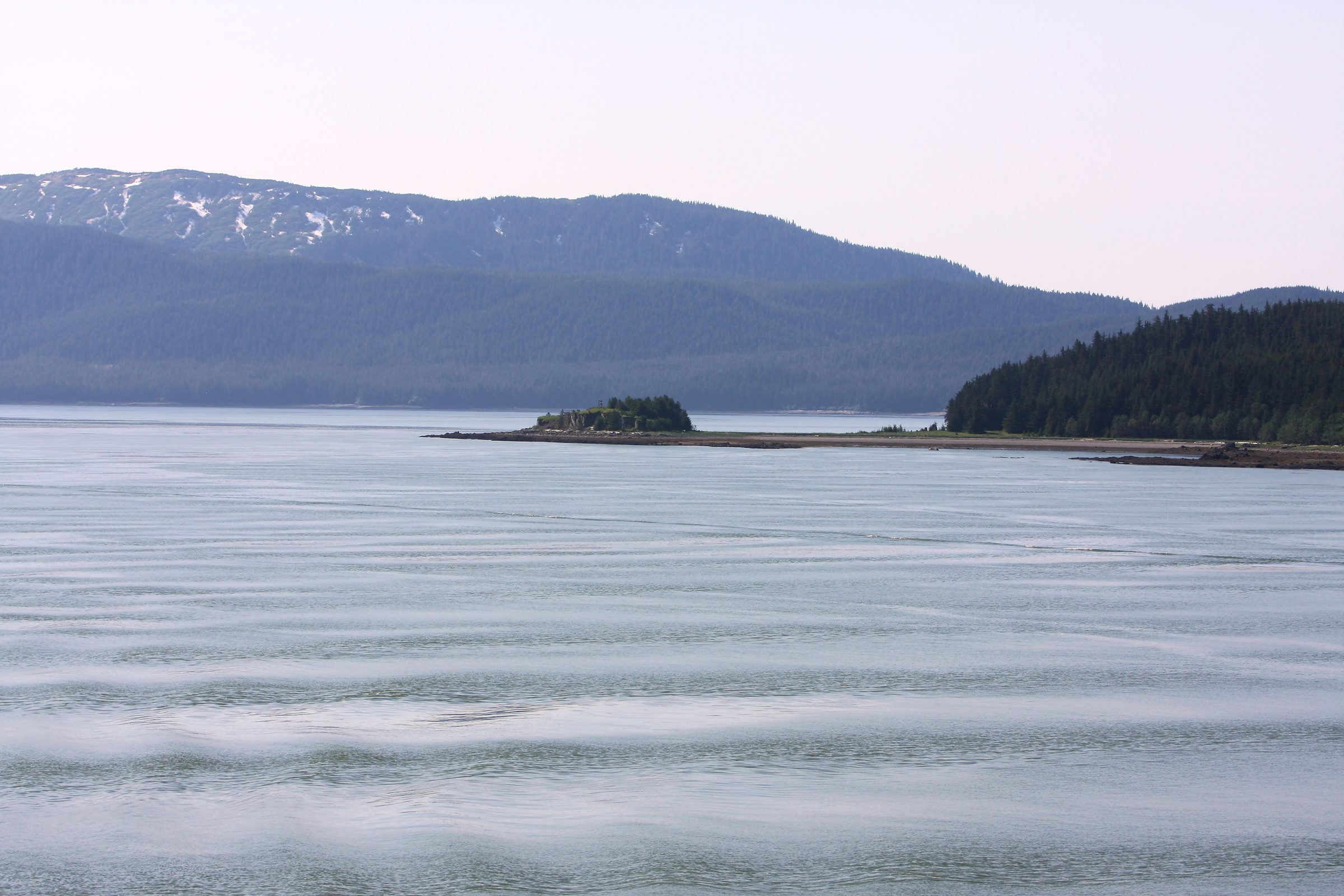 Misty grey water with distant blue mountain ridges under low cloud.