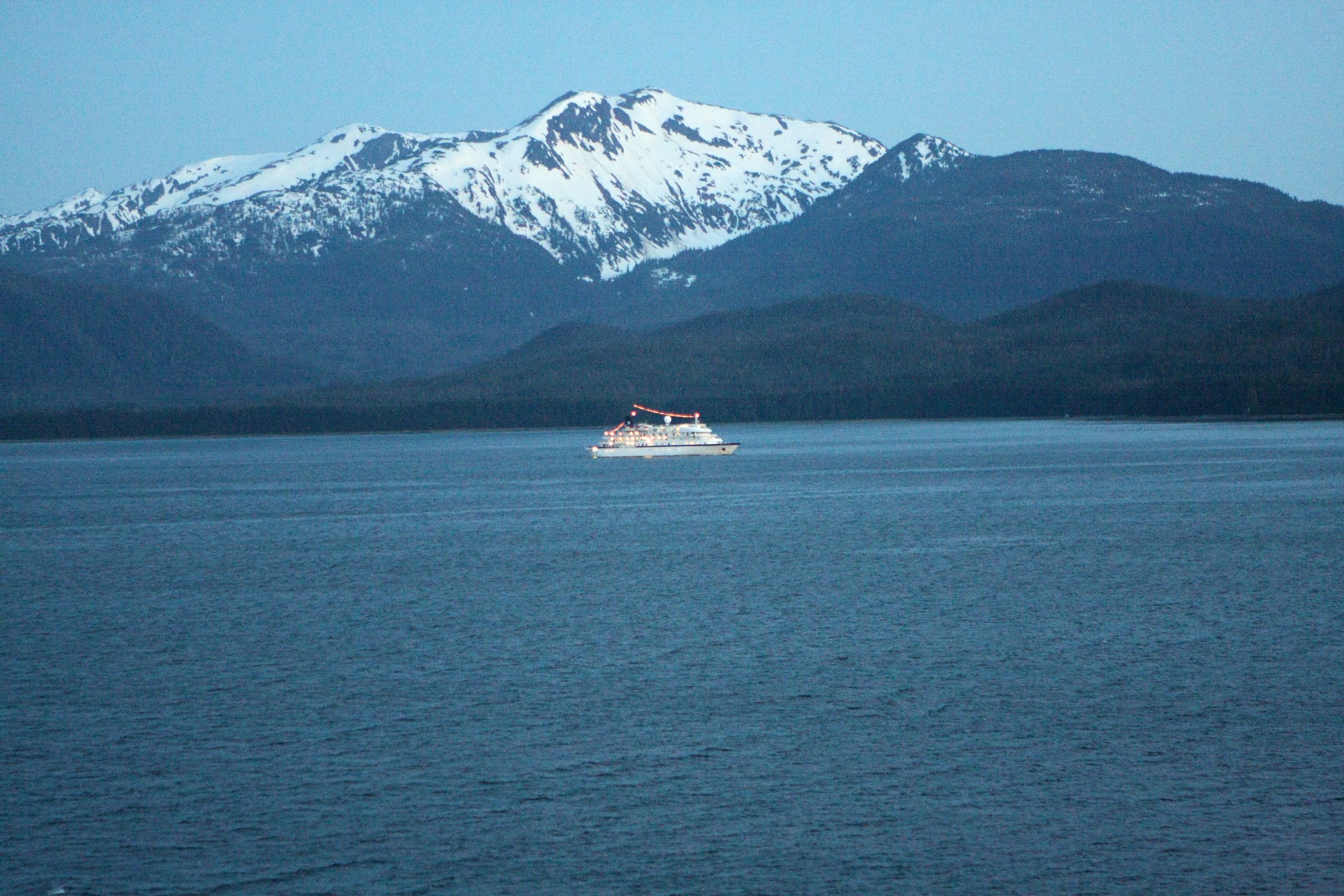 Small white ferry crossing a deep blue bay toward snowy mountains.
