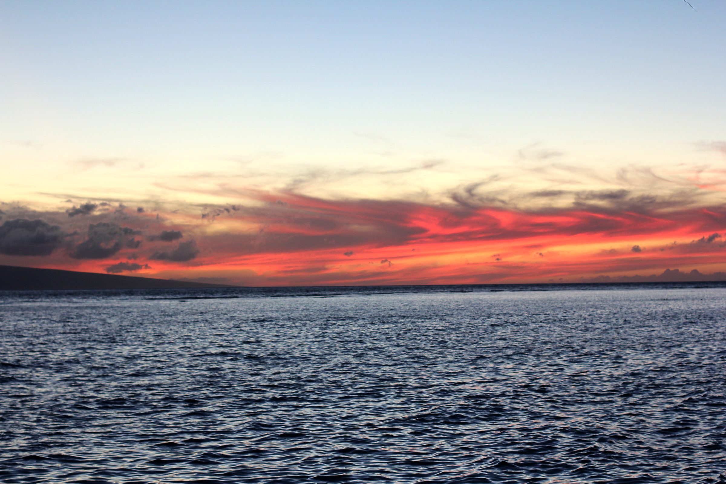 Thin magenta band of sunset cloud over a dark ocean.