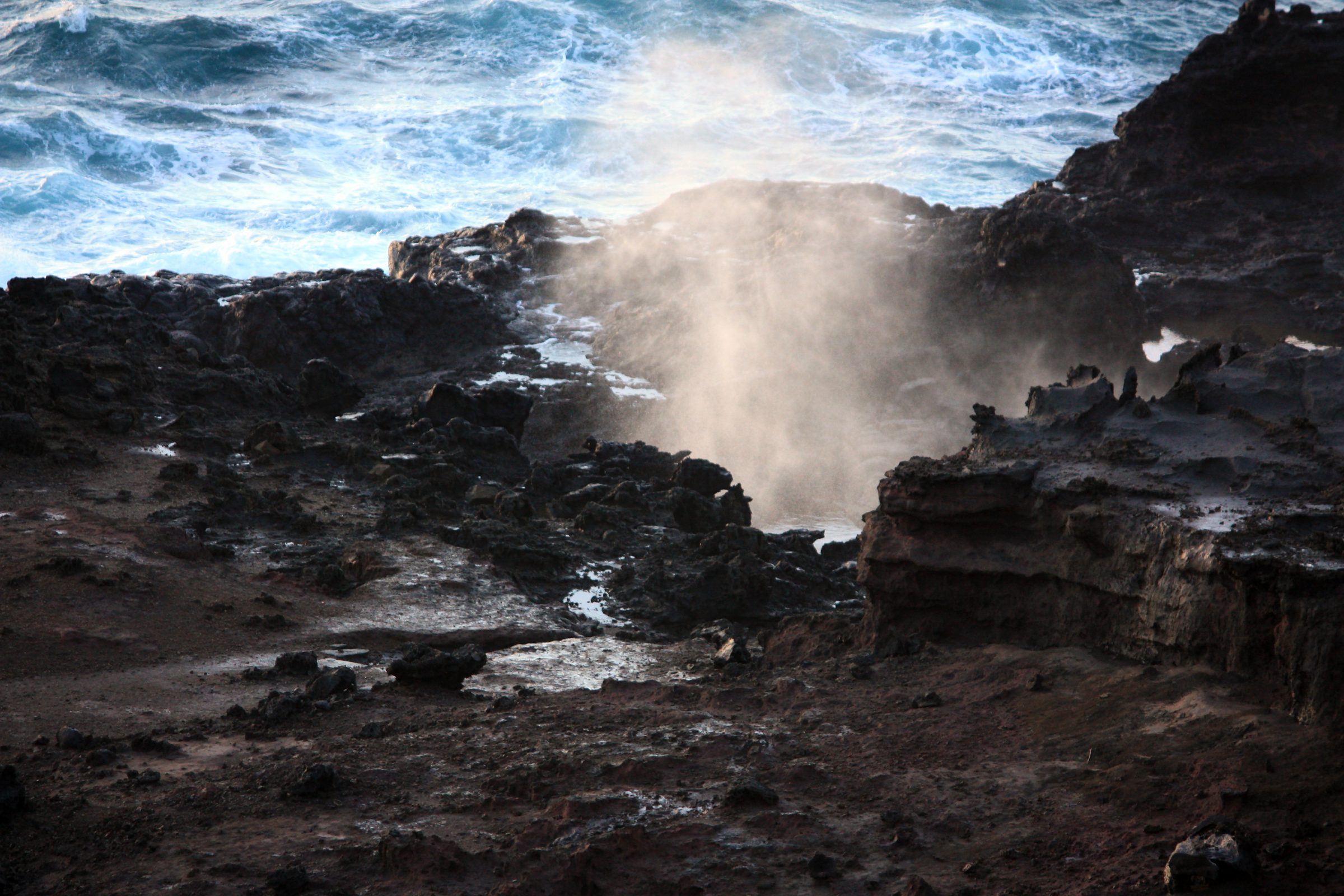 Sea spray exploding from dark jagged volcanic rocks.