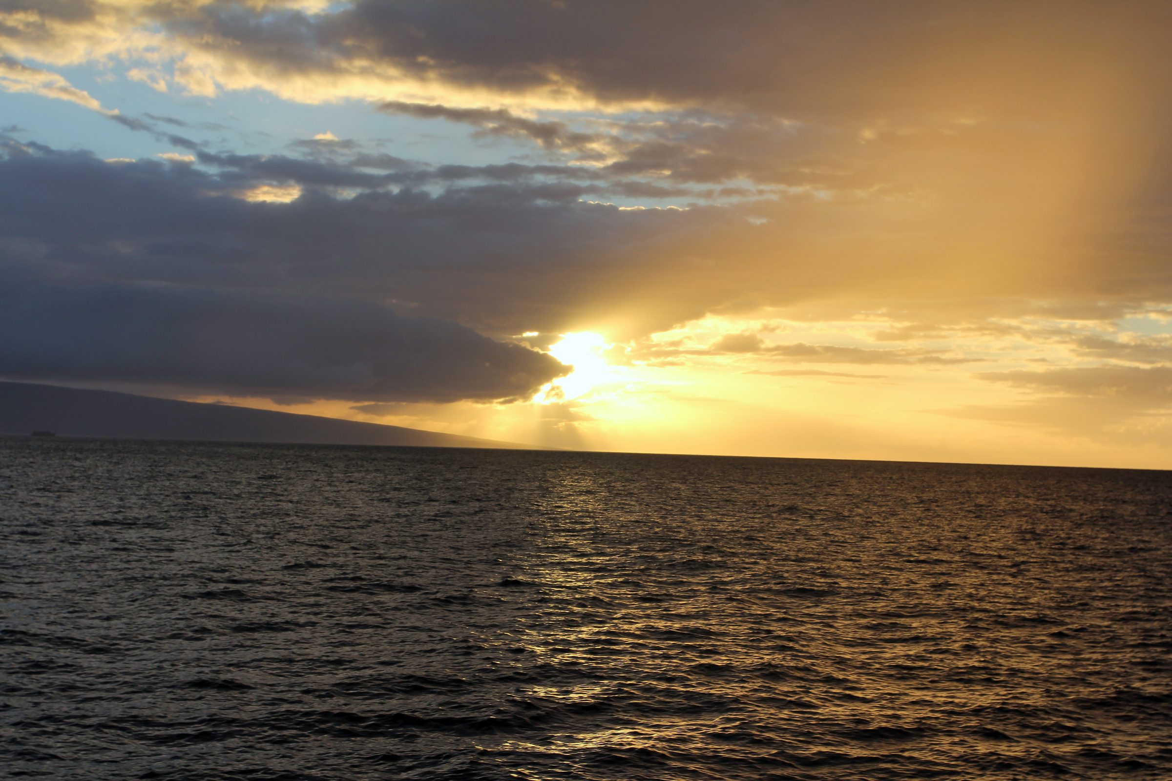 Sun rays breaking through heavy dark clouds onto the ocean.