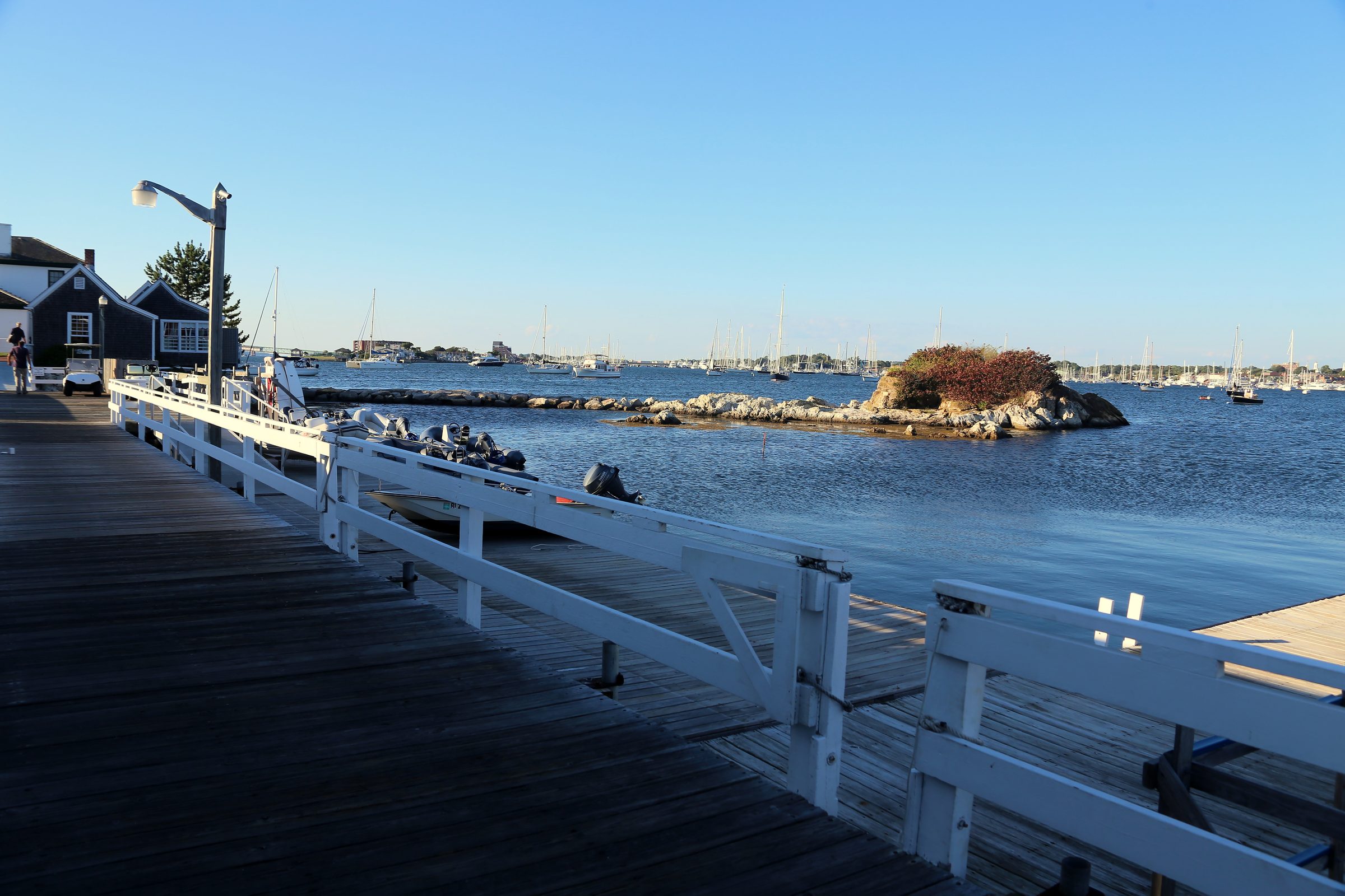 White boardwalk and pier looking toward boats and a distant island.
