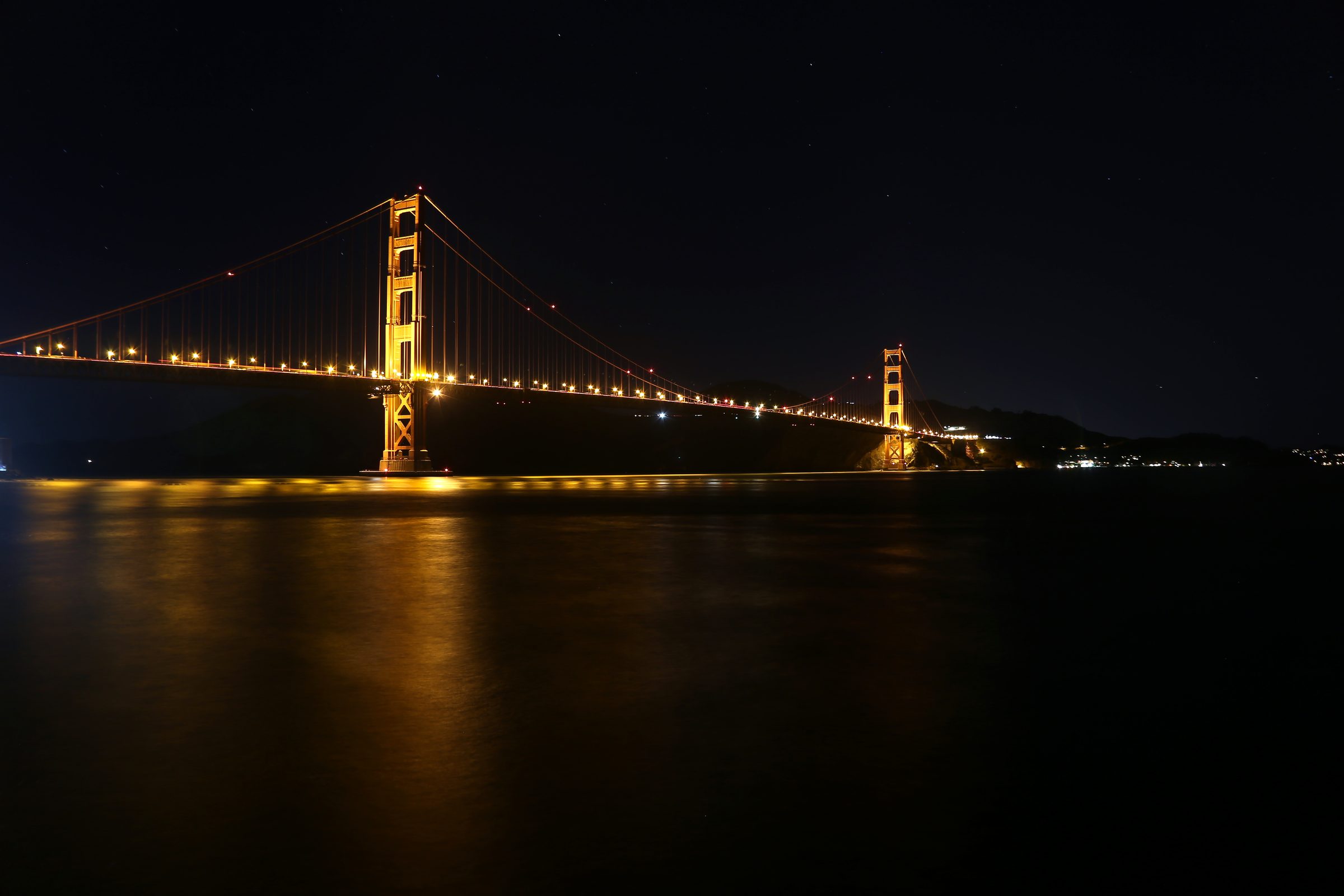 Golden Gate Bridge lit orange at night reflecting in dark water.