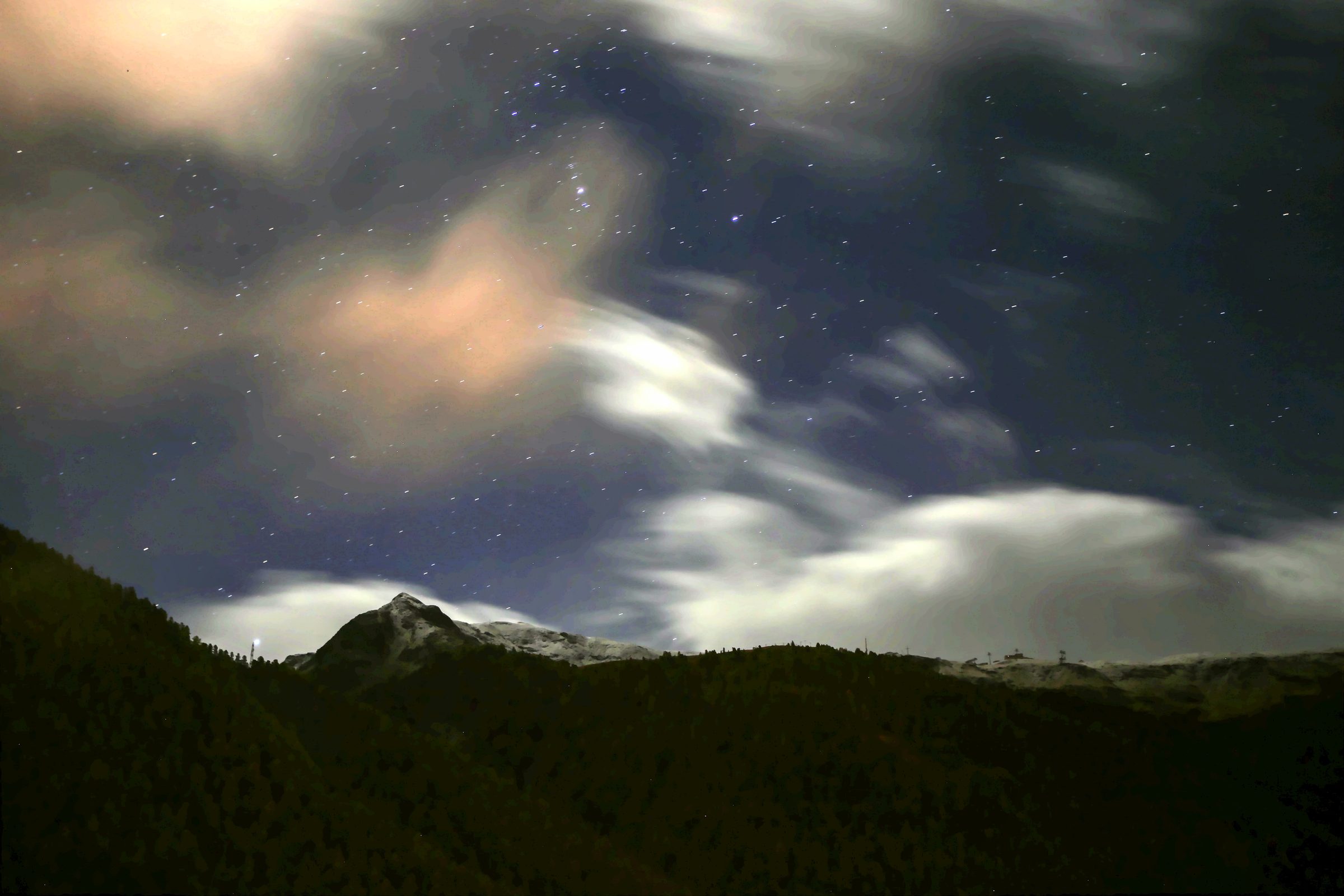 Starry night over a dark forest ridge with pale streaking clouds.