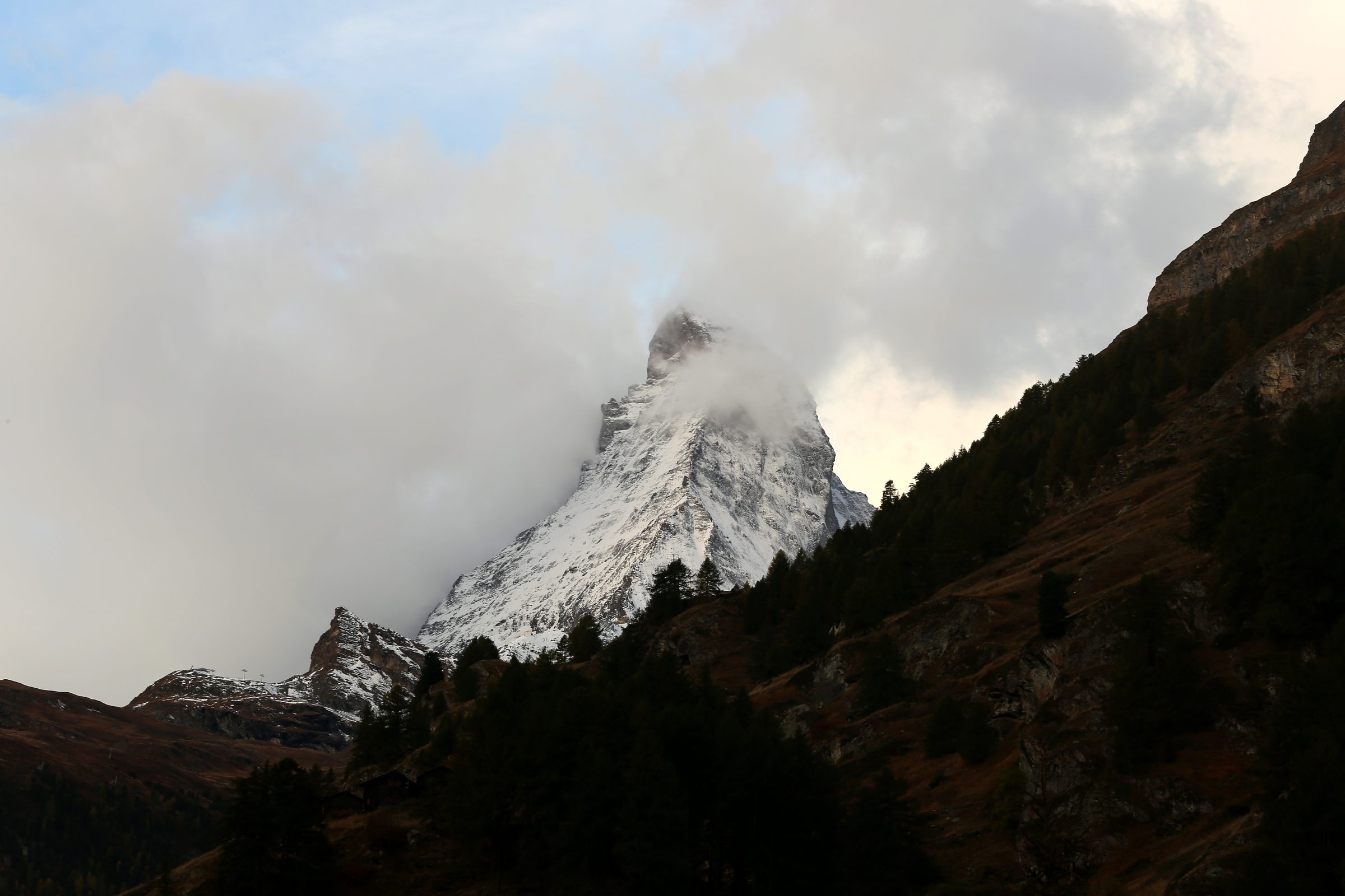 Snowy peak emerging from mist above a dark forested slope.