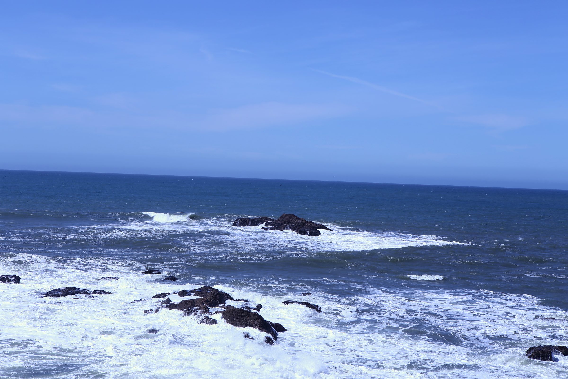 Rough blue ocean and white surf among dark coastal rocks.
