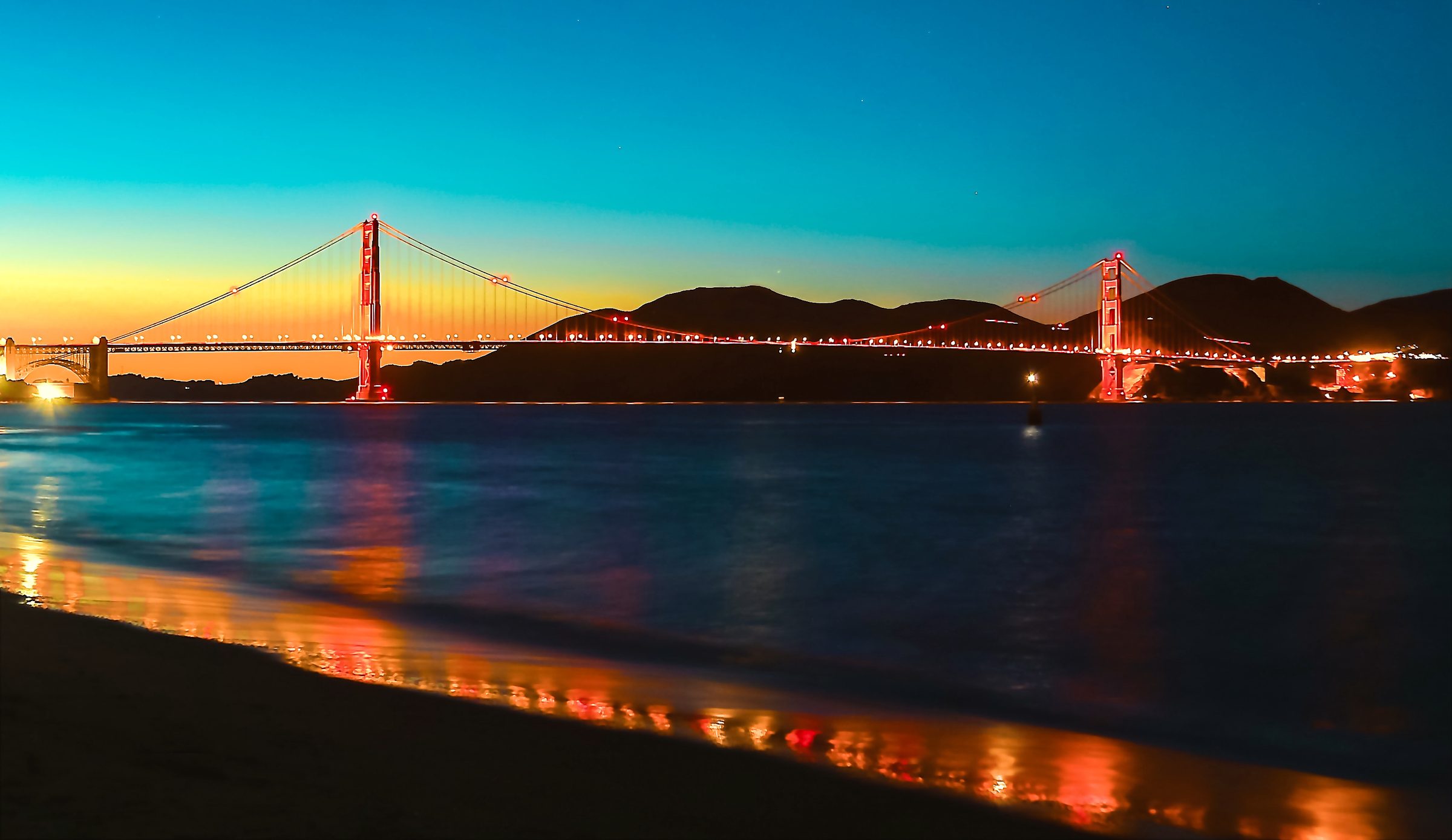 Golden Gate at dusk with orange light streaking wet sand.