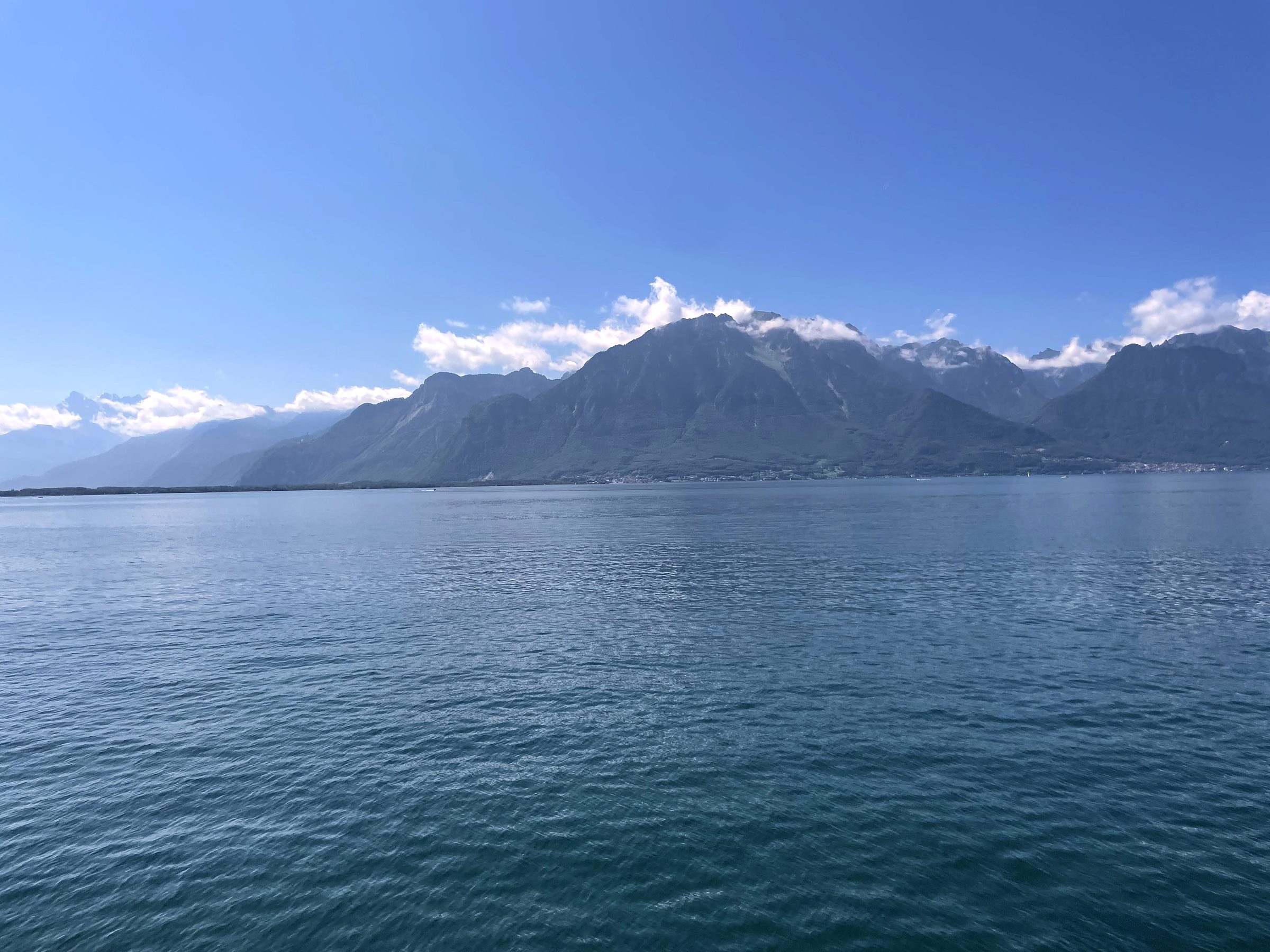 Open teal lake fetching toward distant clouded mountain peaks.