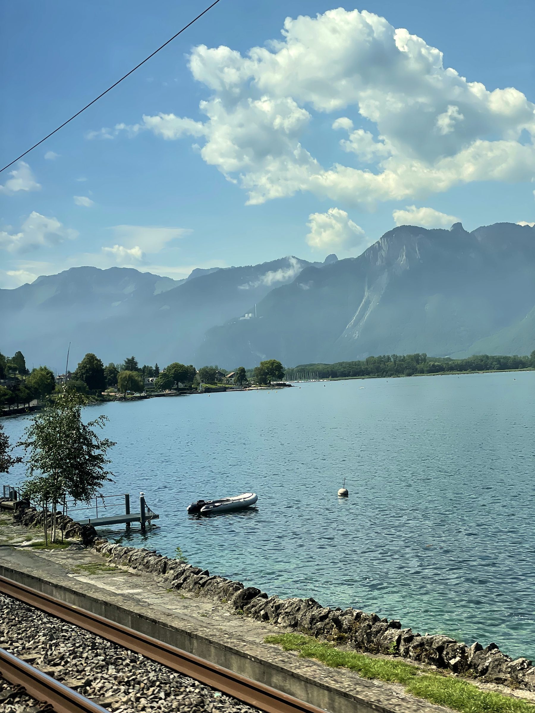 Railway tracks pointing toward a lake and misty blue Alps.