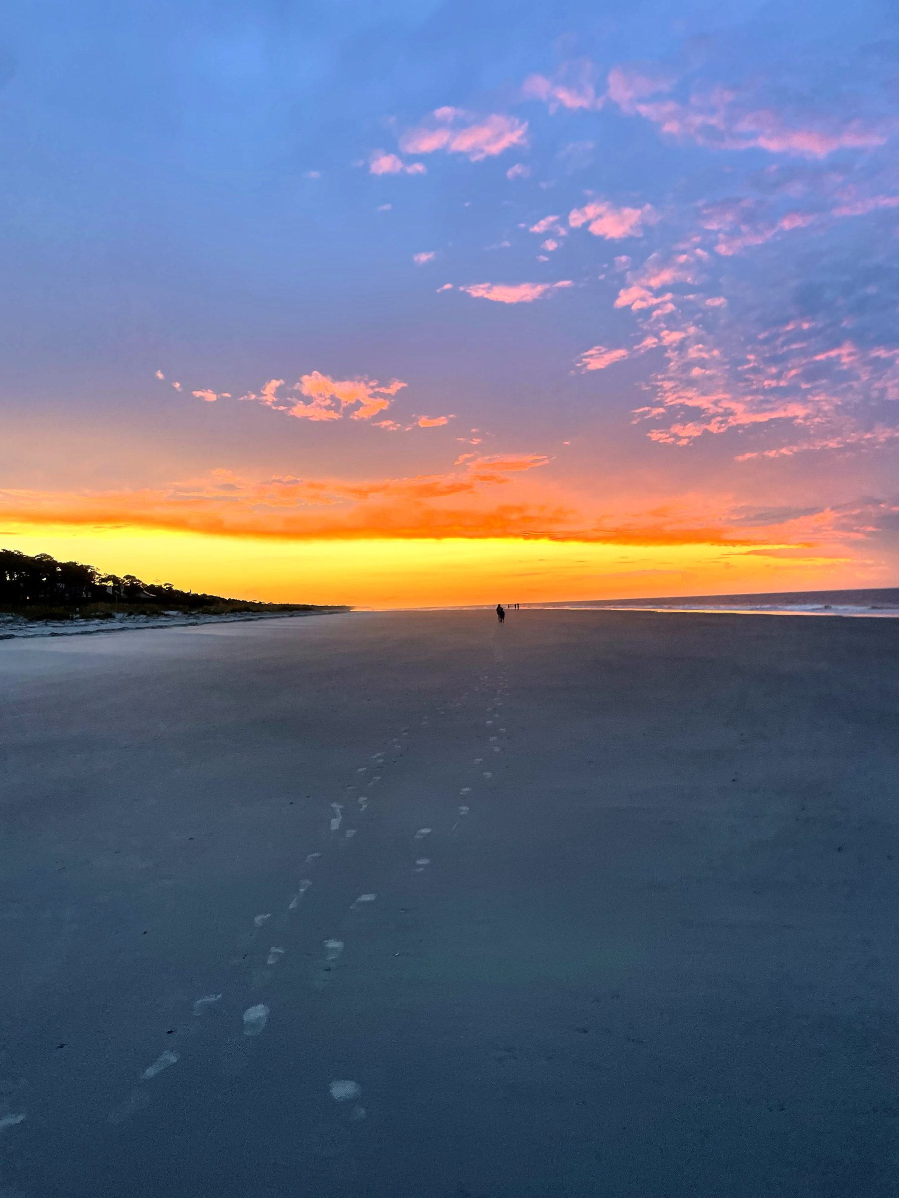 Footprints in sand leading toward pink and magenta sunset clouds.