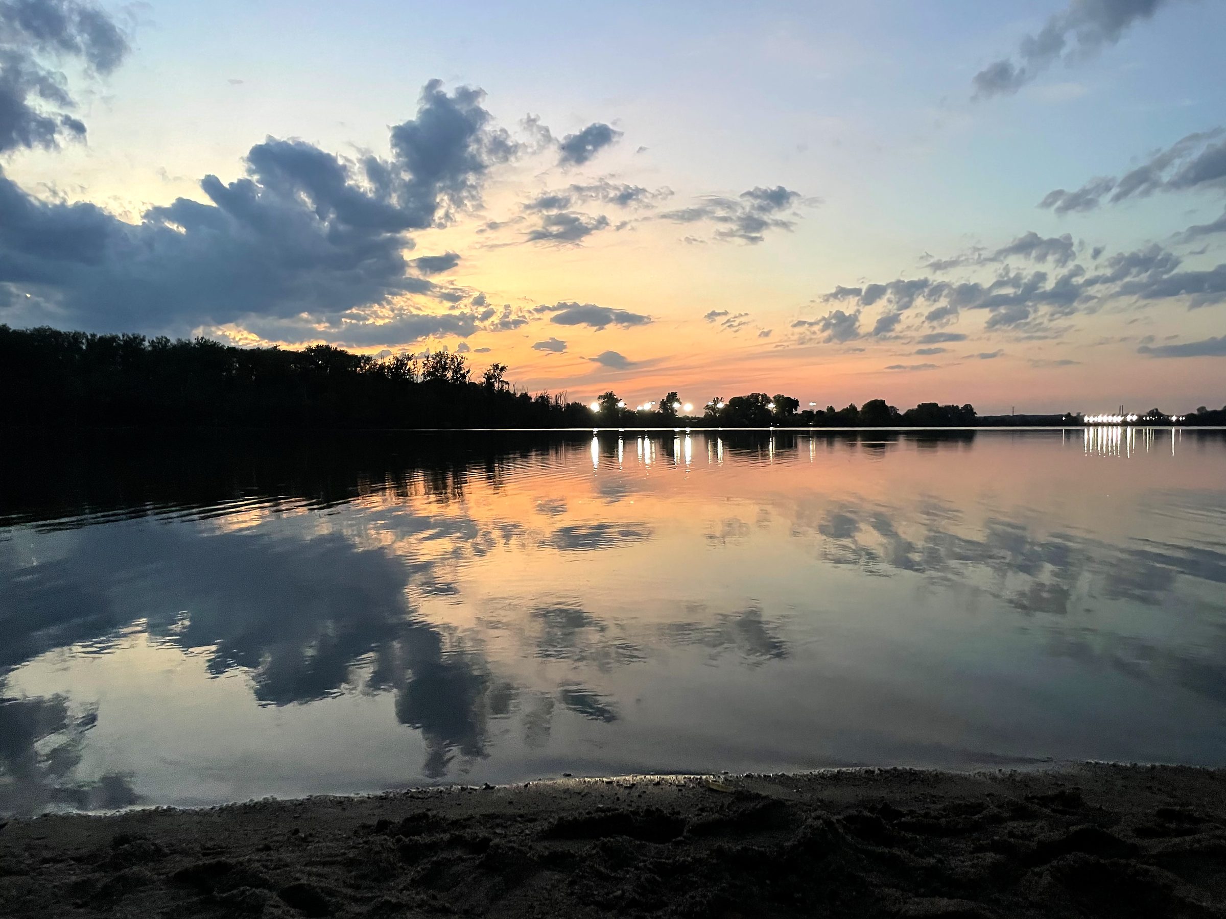 Glassy dusk lake reflecting clouds with soft shoreline.