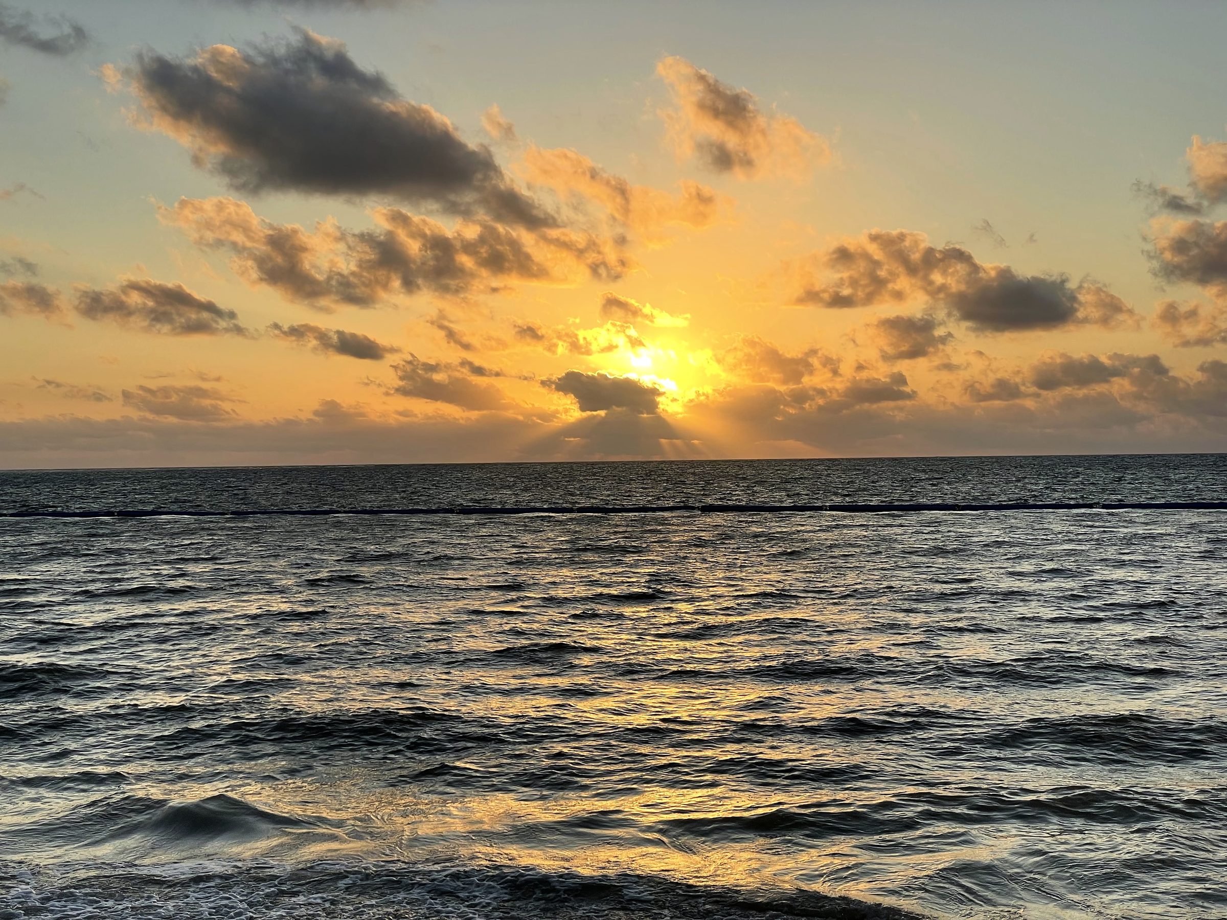 Textured golden clouds and sun over a choppy open sea.