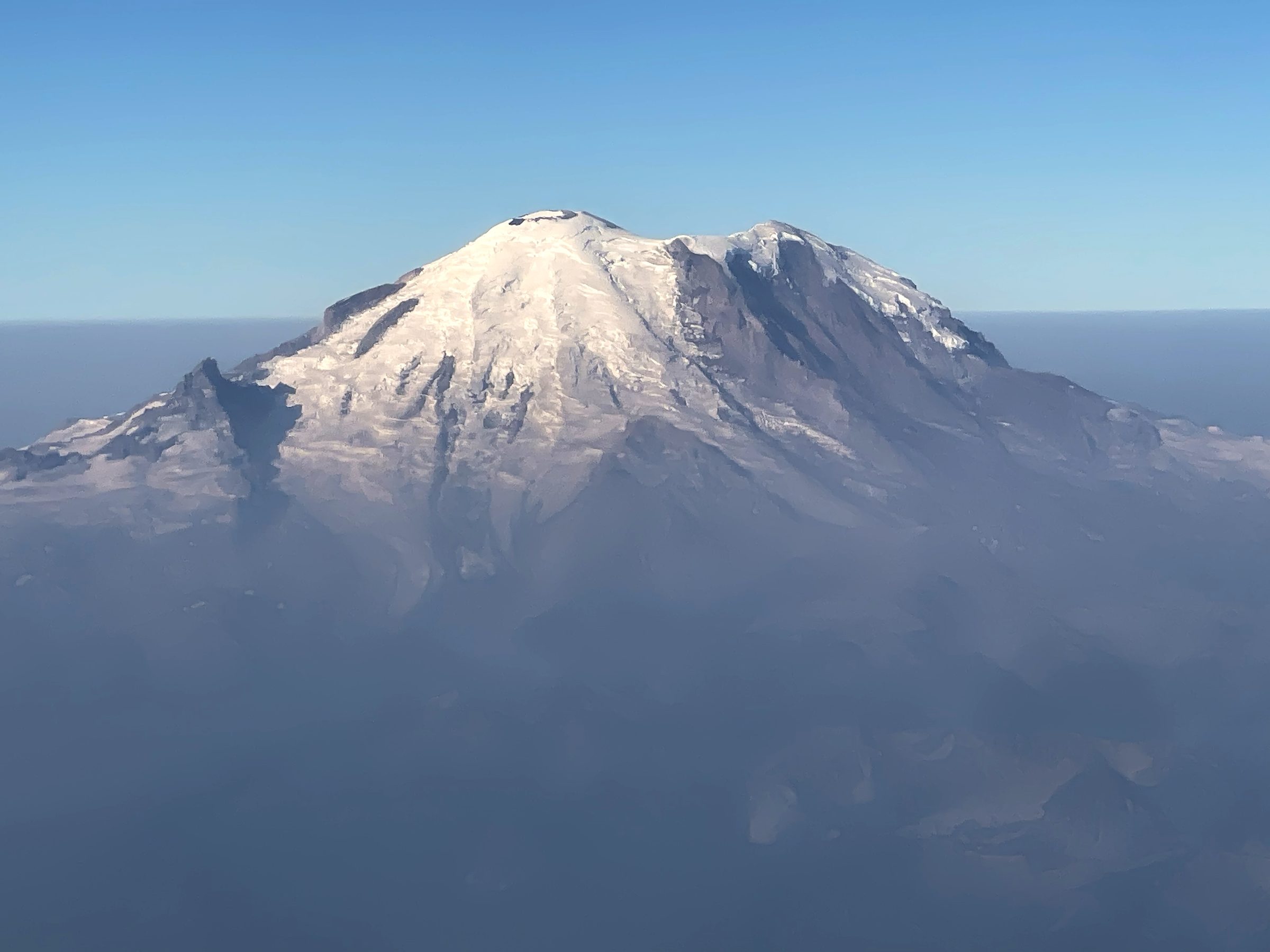 Snow-capped glacier dome rising above a thick haze layer.