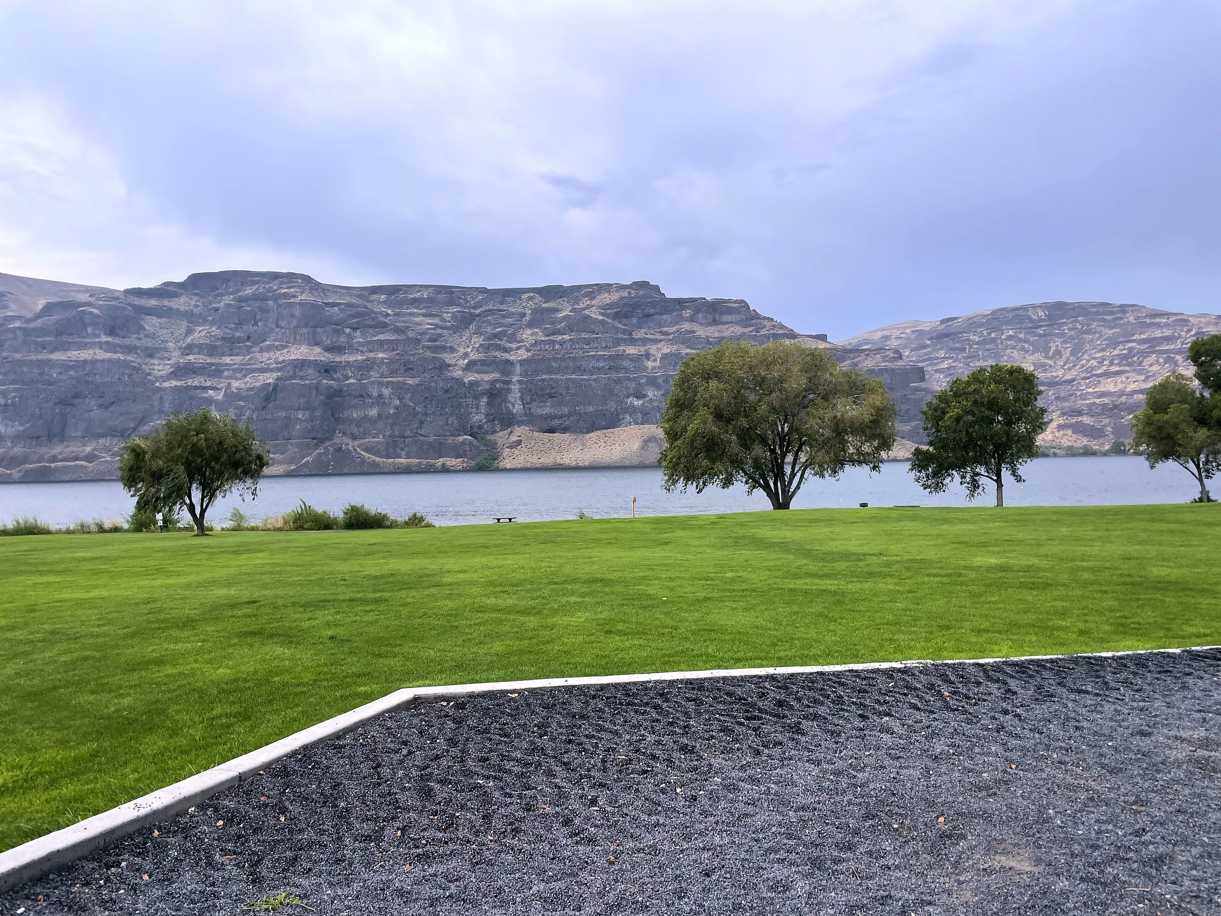 Manicured park grass and patio against layered mesa cliffs.