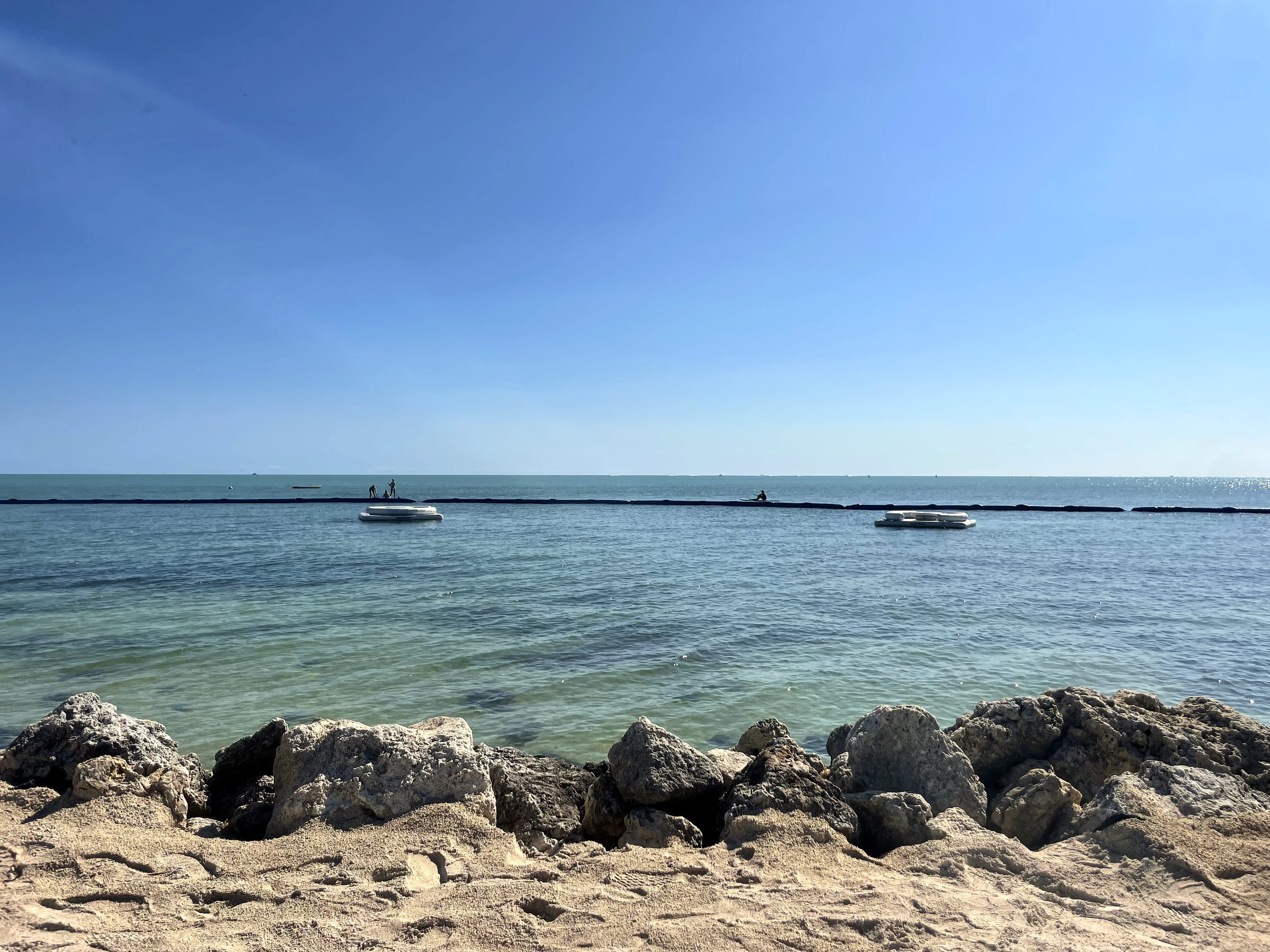 Rocky riprap shore with twin swim rafts on clear turquoise water.