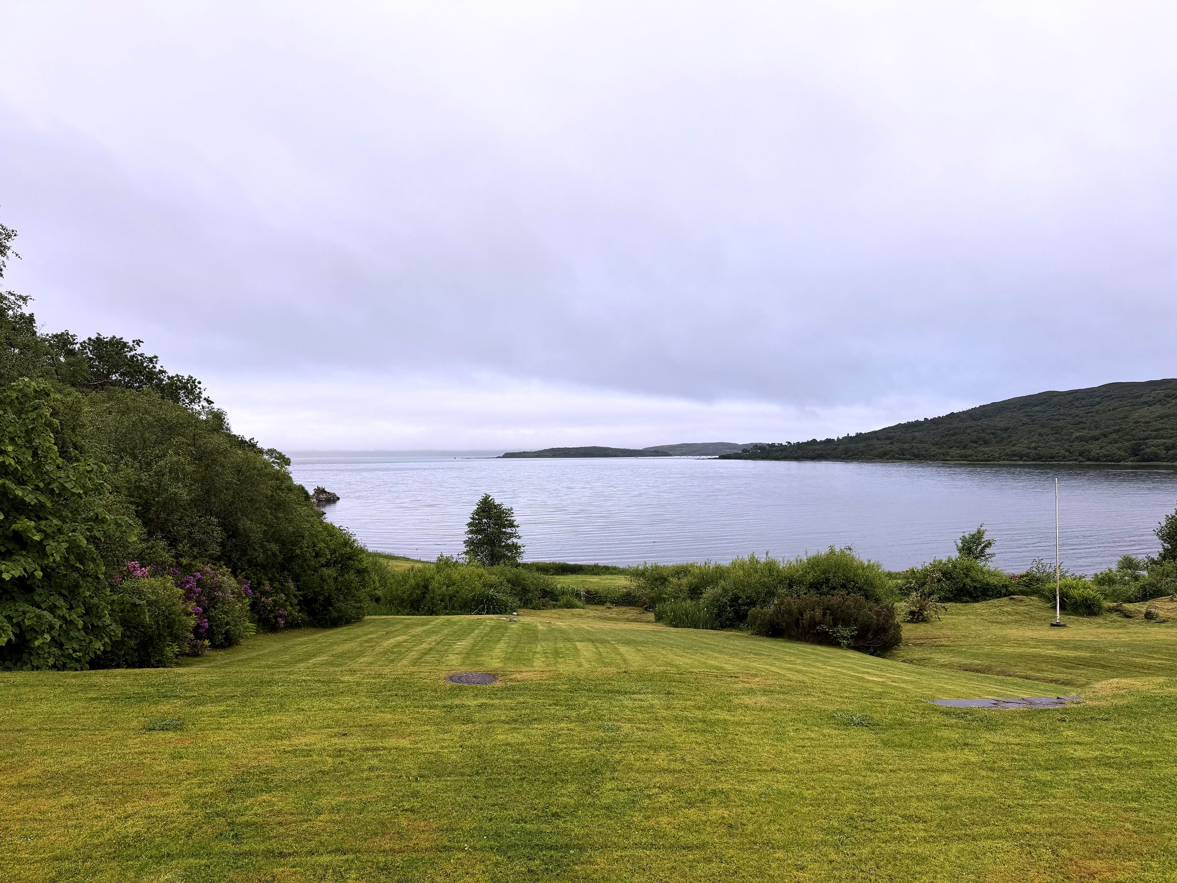 Striped green lawn leading to a silver bay under overcast sky.