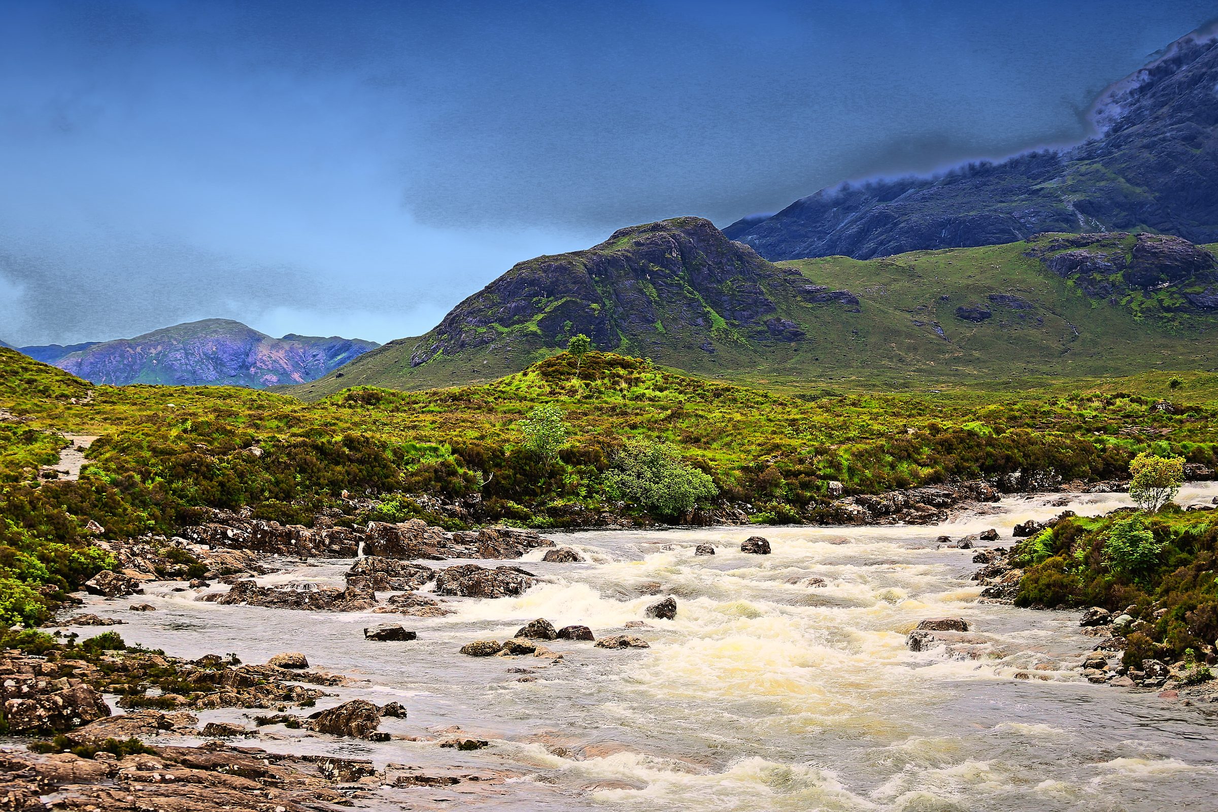 Pale rushing flood of a rocky stream under stormy highland hills.