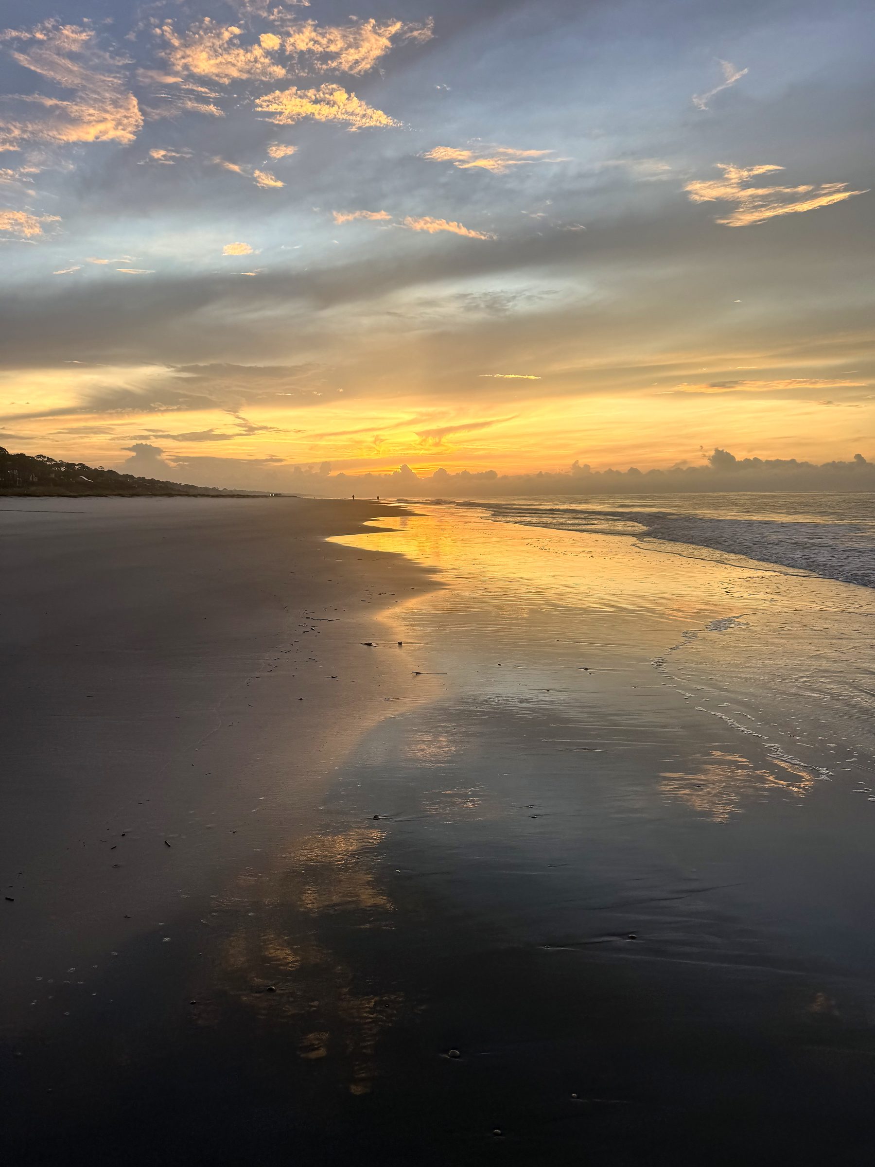 Wet sand mirroring gold and blue twilight along a quiet shore.