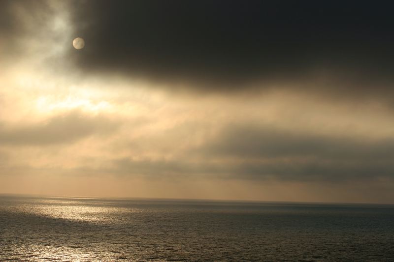 Golden sun behind dark clouds reflecting on a calm open sea.