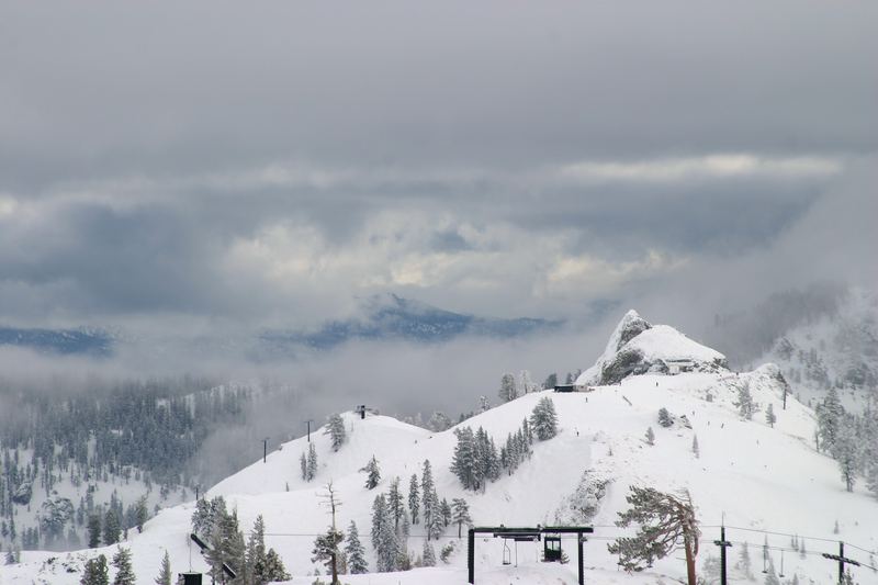 Snowy mountain peak rising from fog with faint ski-lift cables.