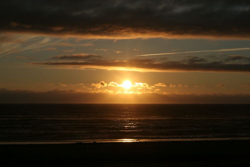 Ocean sunset with a thin contrail crossing a gold sky path.