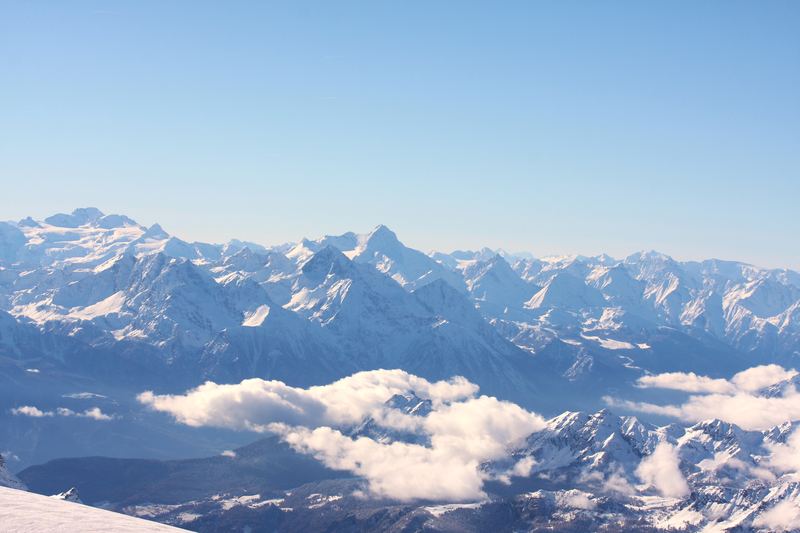 Mountain peaks piercing a flat shelf of clouds from above.