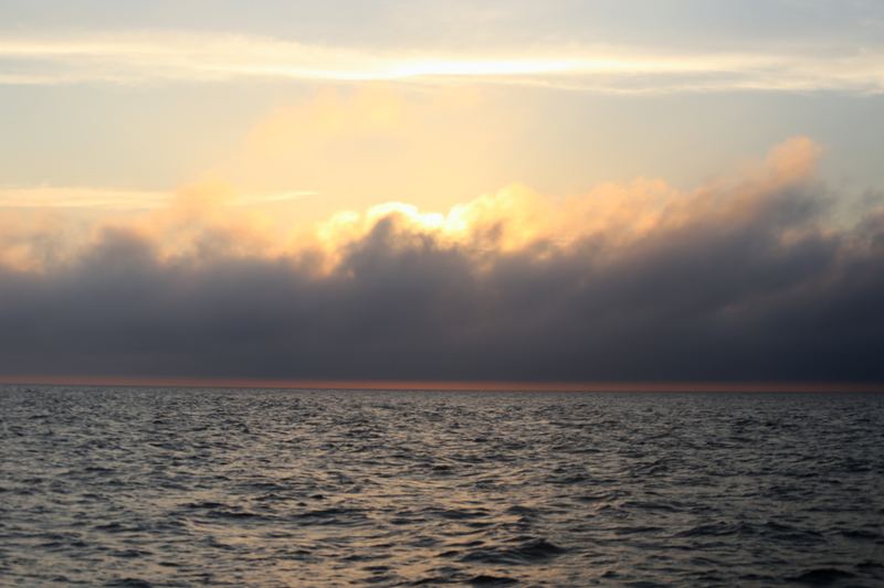 Sun veiled by thick white and grey cloud over dark sea.