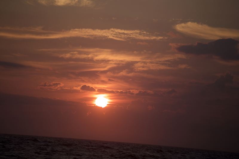 Deep orange sunset orb low over a choppy dark sea.
