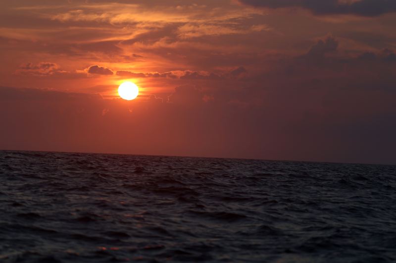 Sun glowing through thin haze over open ocean.