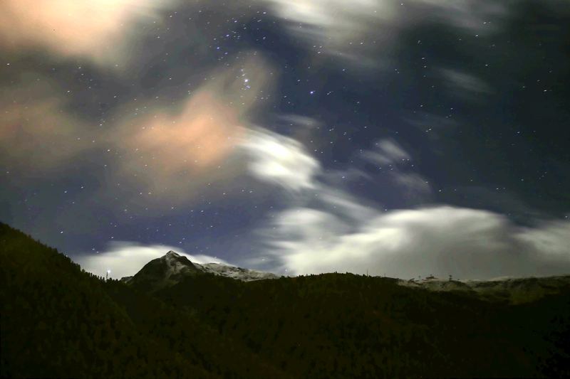 Starry night over a dark forest ridge with pale streaking clouds.
