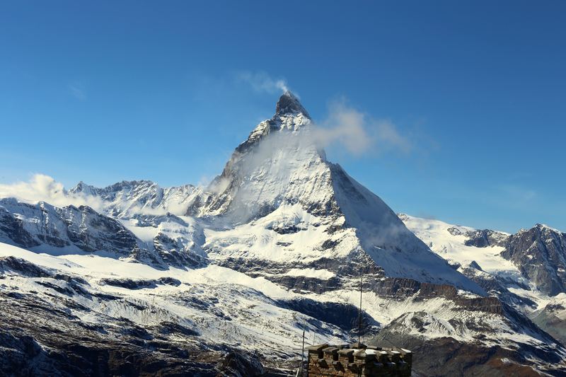 Snowy Matterhorn range under clear blue with a hut roof corner.