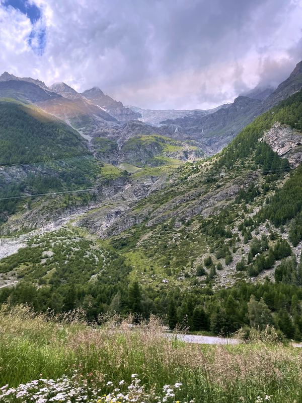 Rocky alpine valley with snow patches and green wildflower slopes.