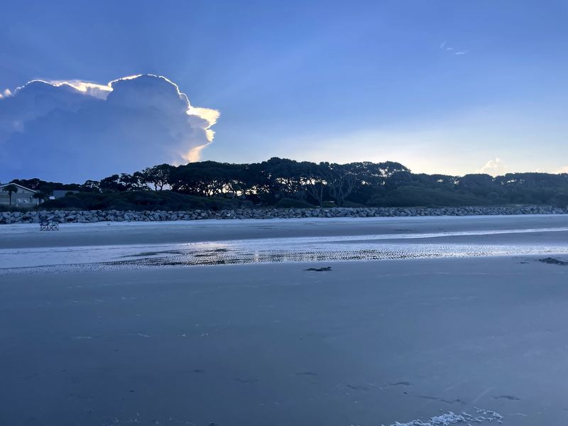 Wide low-tide beach with sandbars under deep cloudy blue sky.