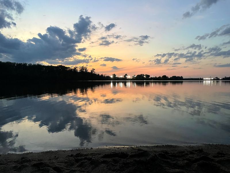 Glassy dusk lake reflecting clouds with soft shoreline.