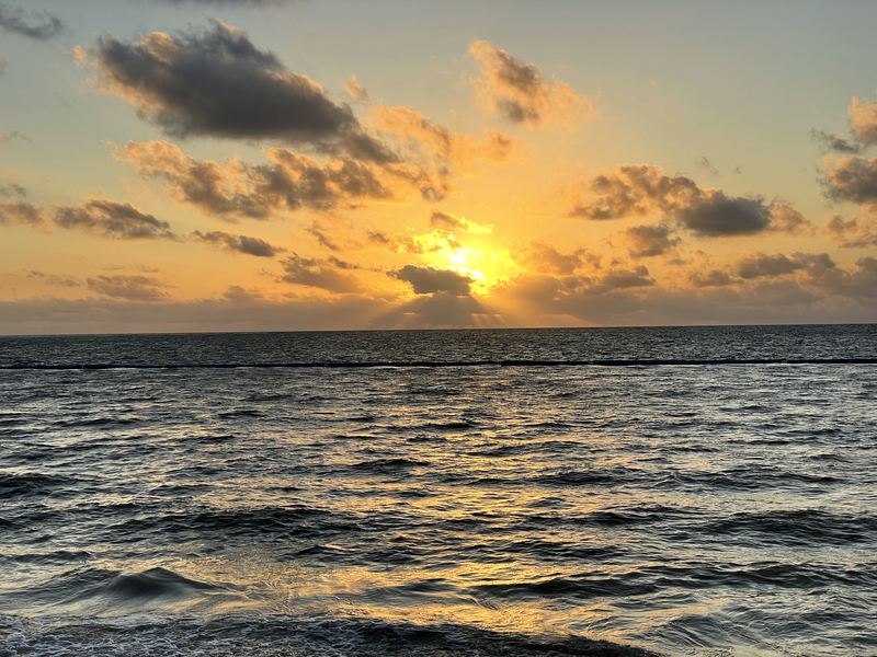 Textured golden clouds and sun over a choppy open sea.