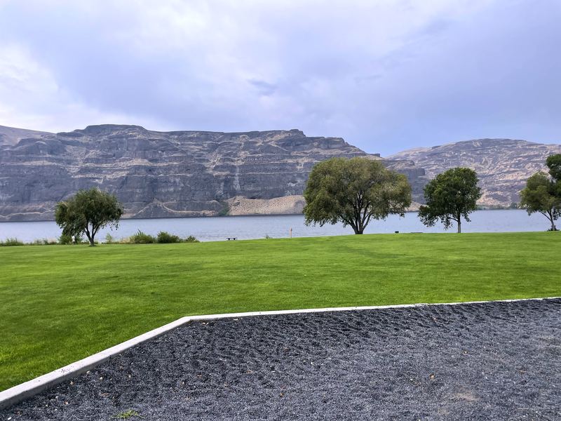 Manicured park grass and patio against layered mesa cliffs.