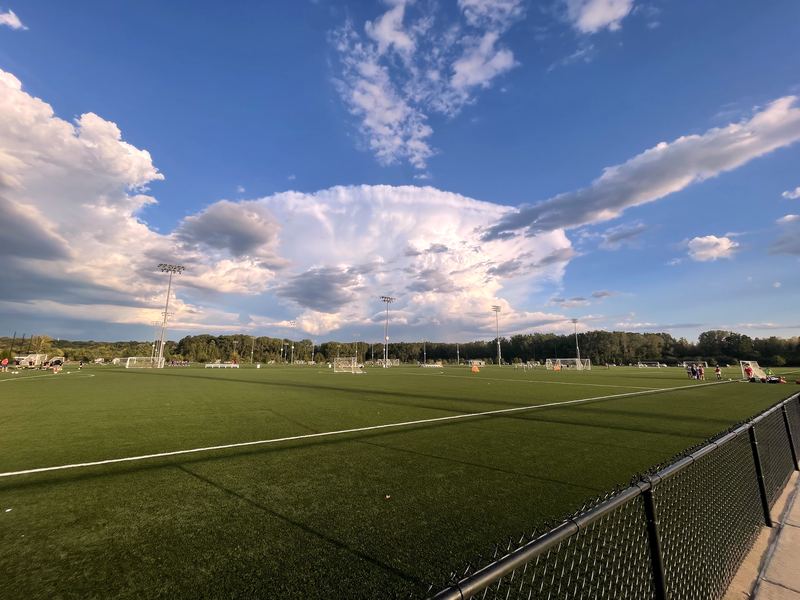 Green turf sports fields under a dramatic anvil thundercloud.