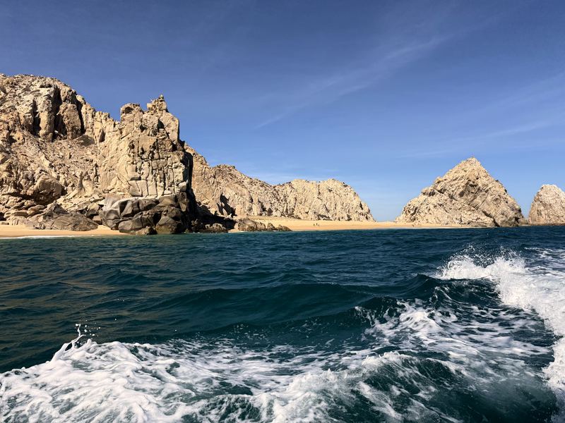 Boat wake aiming toward twin coastal sea stacks and beach.