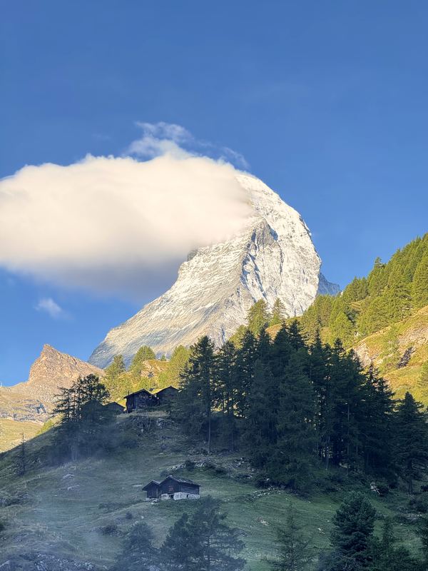 Matterhorn with a banner cloud above green chalets and trees.